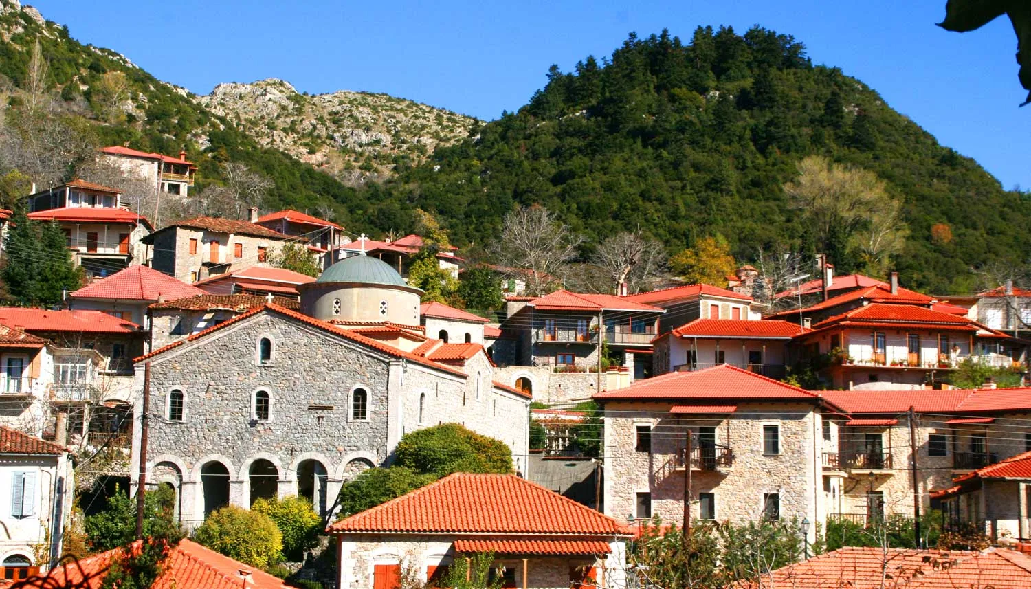 Πέτρινα σπίτια με κόκκινα κεραμίδια και εκκλησία κάτω από το βουνό